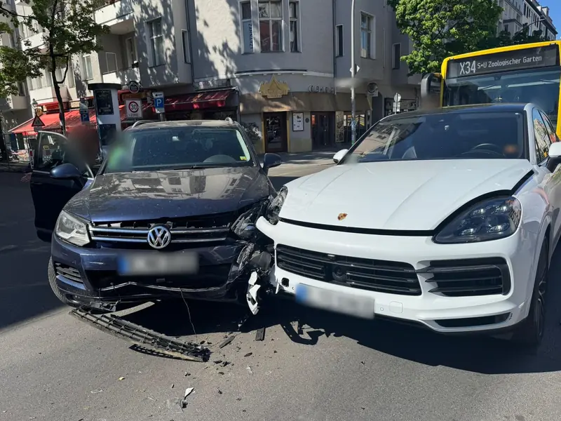 Unfall in Berlin: weißes Porsche-SUV und dunkler VW nach einem Zusammenstoß, beide Fronten beschädigt, Kennzeichen unkenntlich gemacht