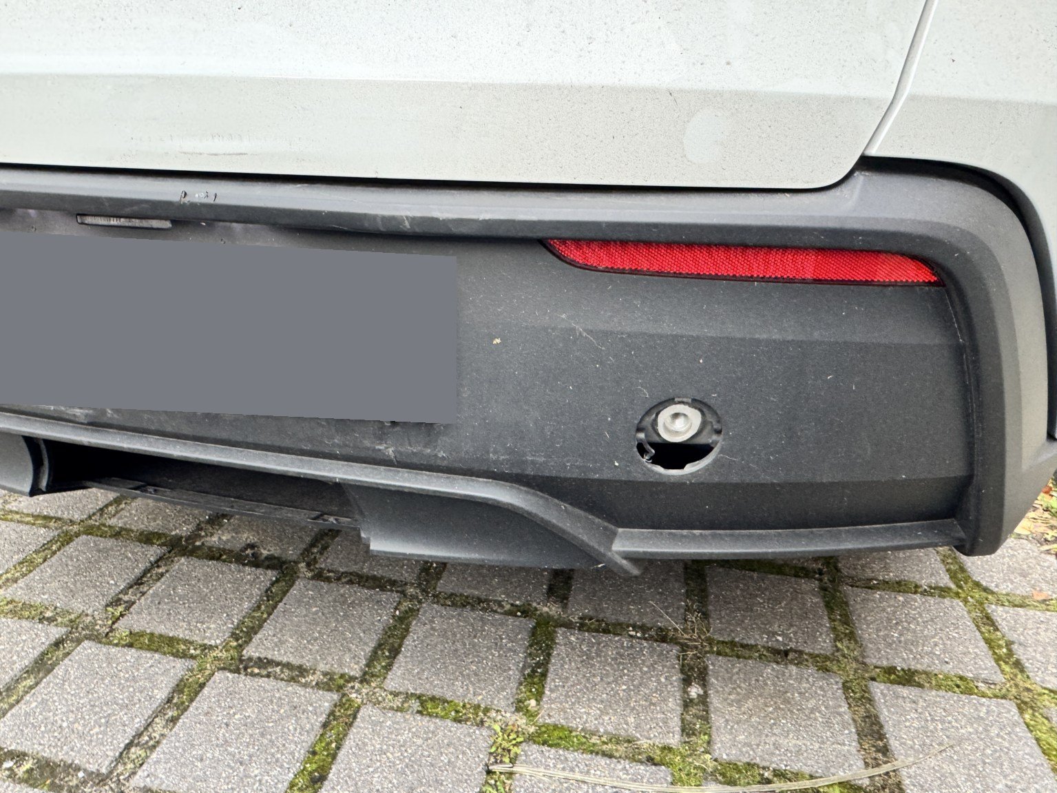 Heckstoßfänger des Tesla Model Y mit beschädigter Abdeckung der Anhängeöse, Kennzeichen unkenntlich gemacht